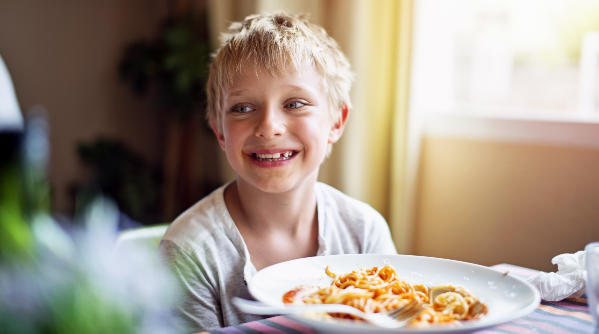 Boy smiling while at the table eating a plate of spaghetti.